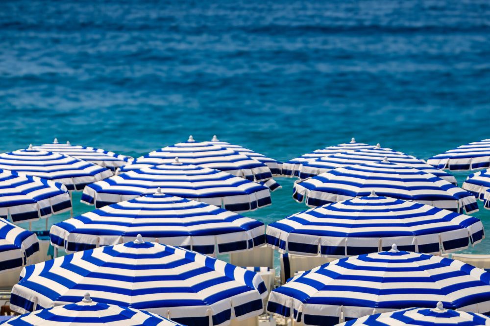 Pebble beach along Promenade des Anglais with beach umbrellas and chairs with the turquoise water of the Mediterranean Sea in Nice, Cote d'Azur France
